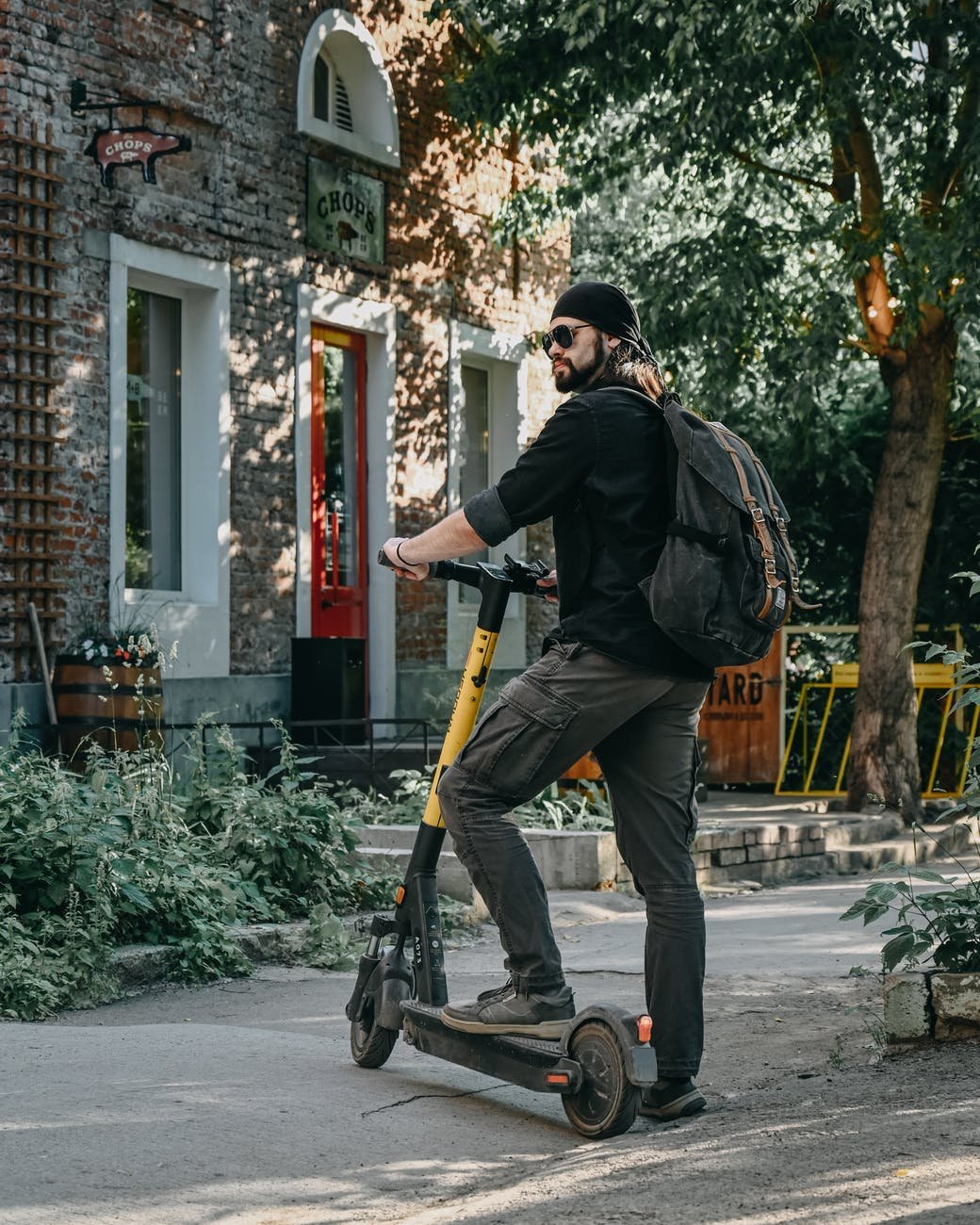 serious man standing on electric kick scooter near old house